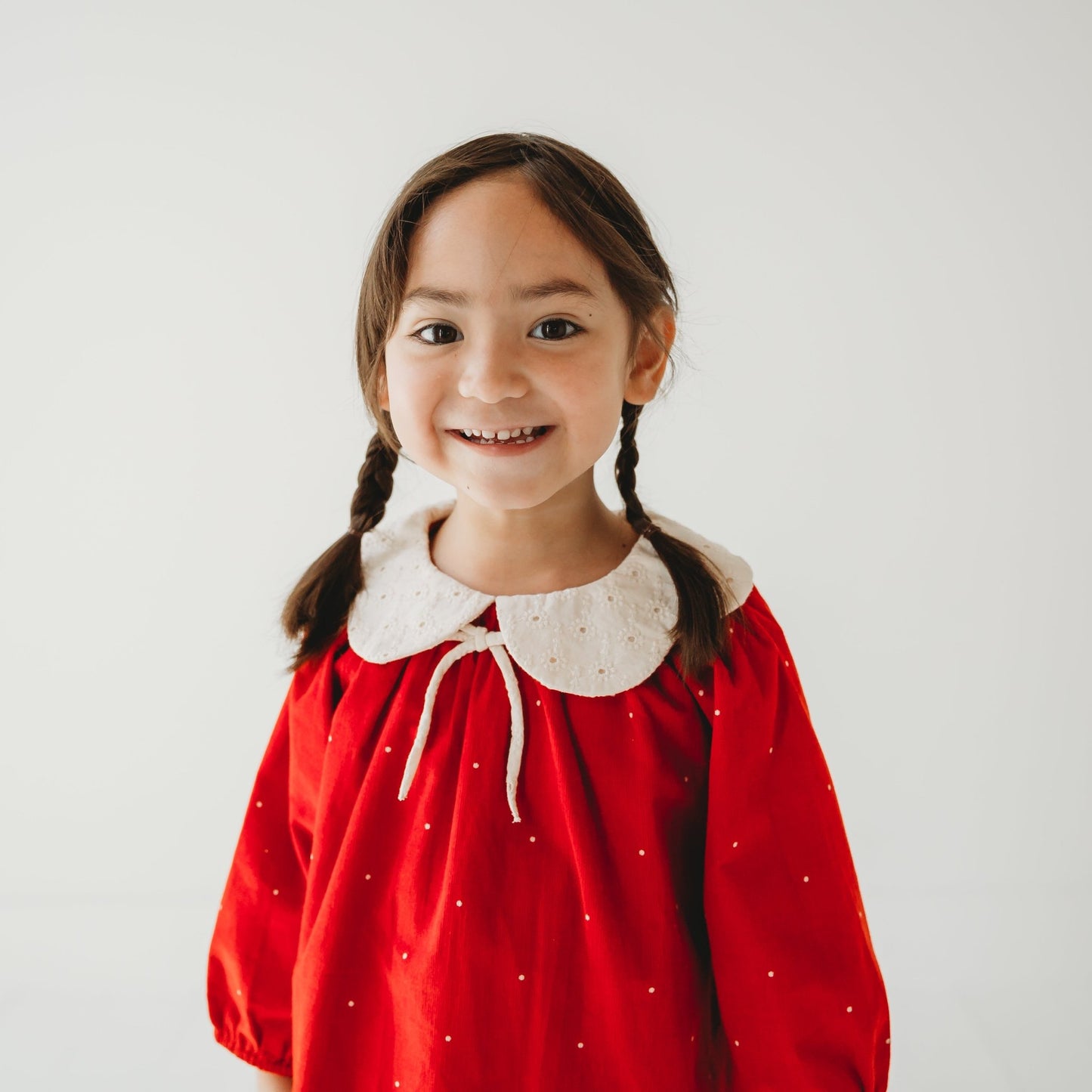 Close up of Girl in LARILI Christmas Carol Red Corduroy Dress with scalloped embroidered collar in a holiday setting.