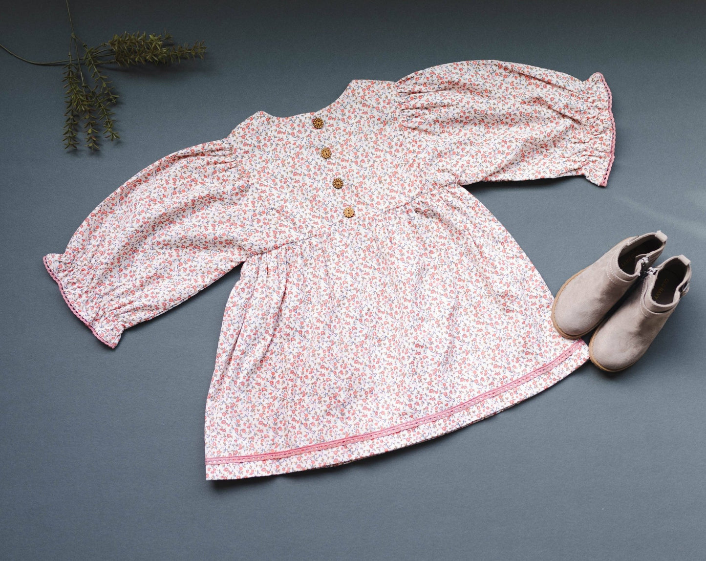 Overhead back view of the LARILI pink ditsy print corduroy dress, highlighting the soft fabric texture, floral patterns, and lace detailing and wooden buttons.