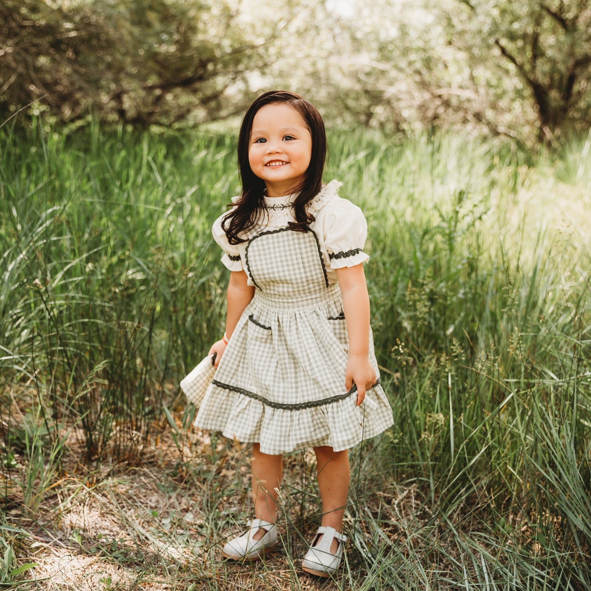 Little girl wearing LARILI green gingham pinafore with embroidered white blouse. 100% cotton outfit for siblings.