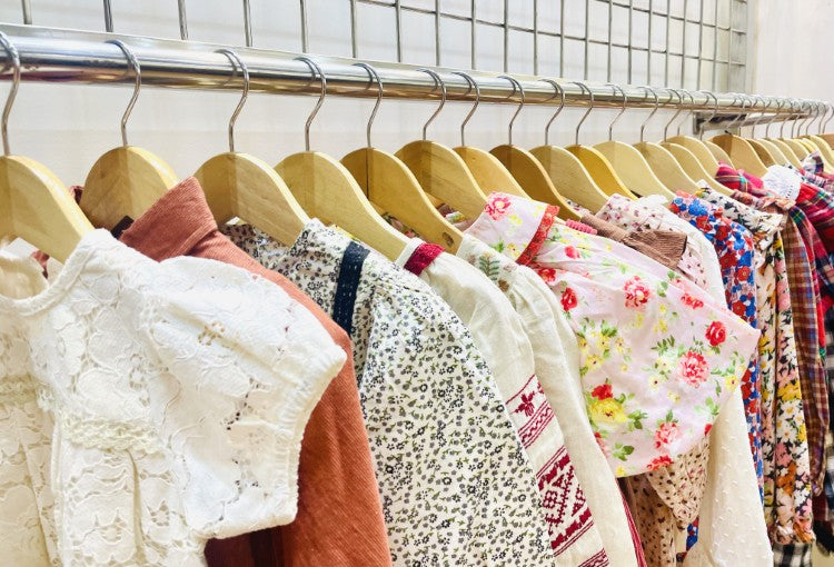 LARILI handcrafted children’s clothing featuring traditional Indian embroidery and block prints on hangers against a decorative tiled wall.