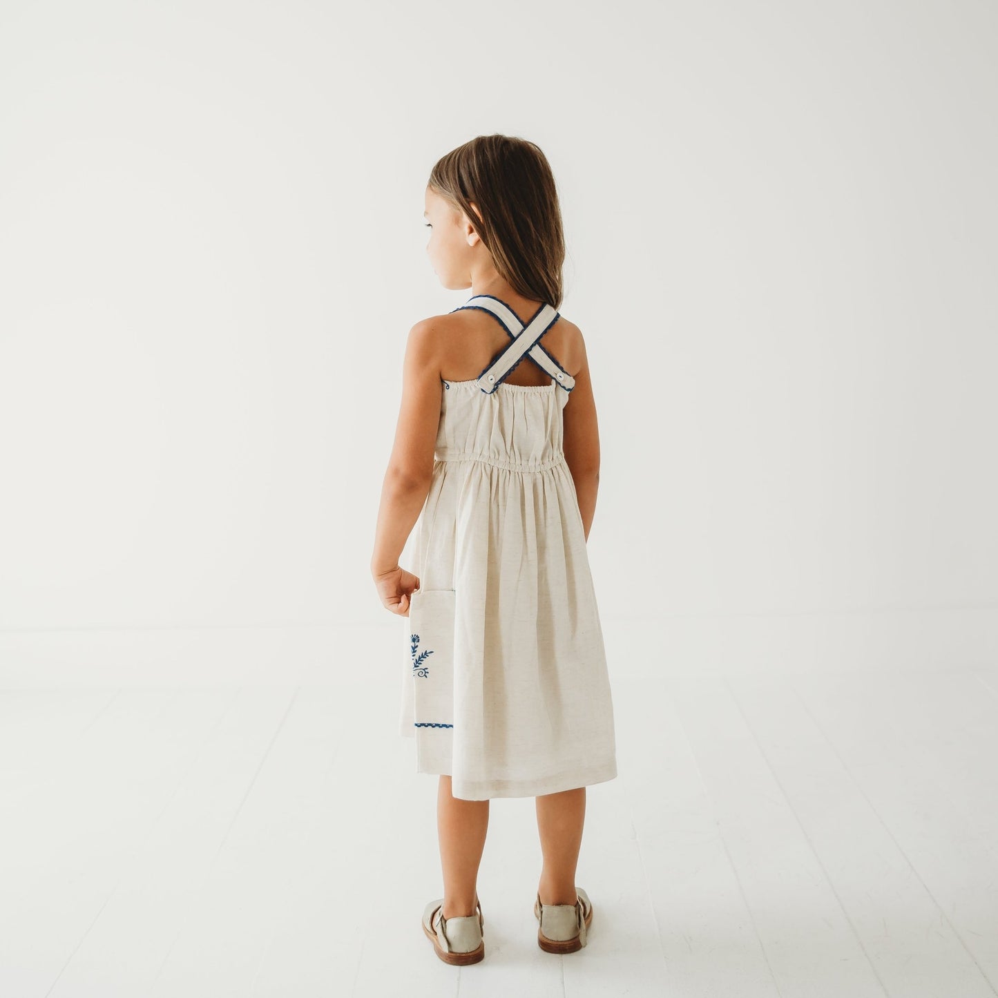 Back view of the Azurea linen dress on a 5-year-old girl, showing the clean finish of the adjustable lace straps.