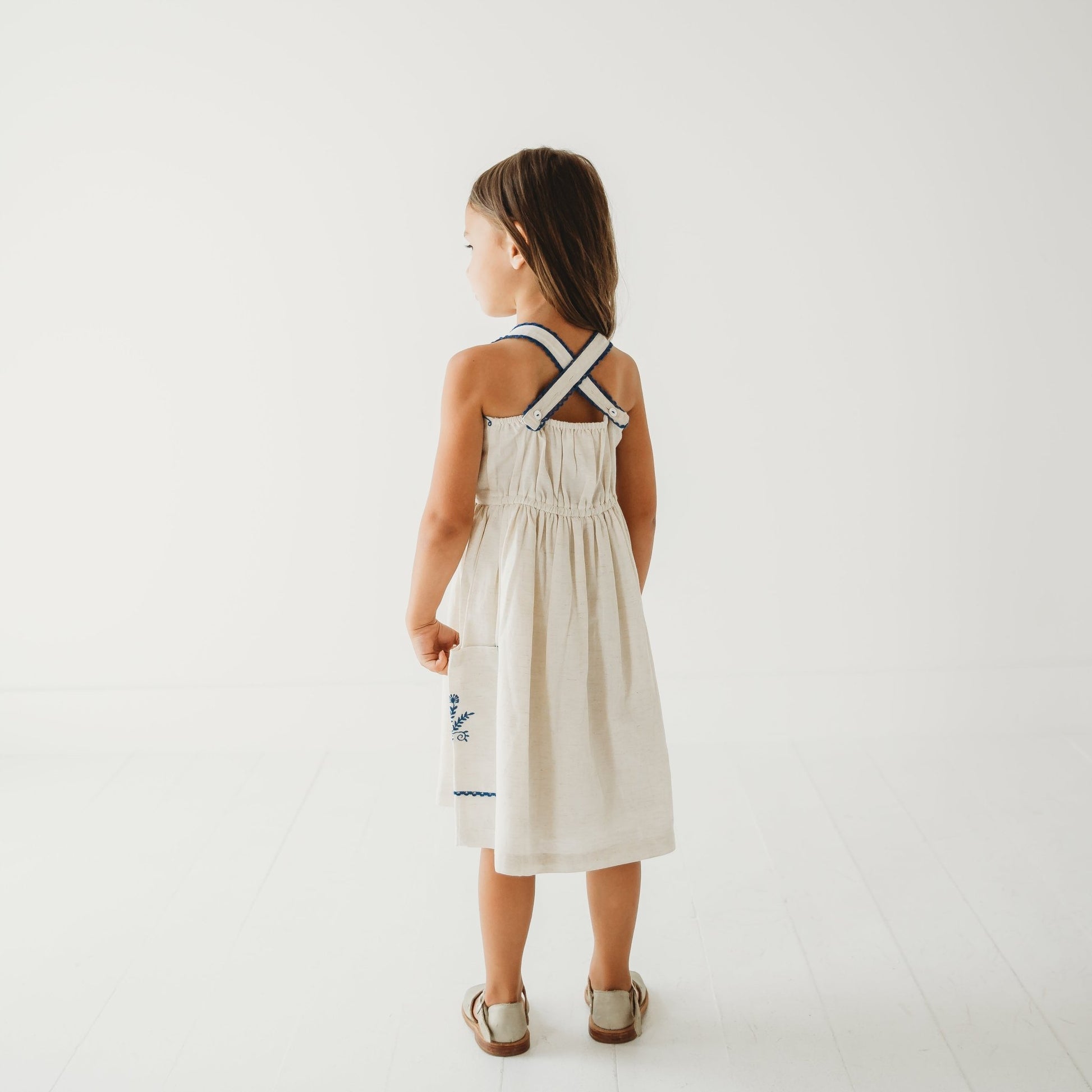 Back view of the Azurea linen dress on a 5-year-old girl, showing the clean finish of the adjustable lace straps.