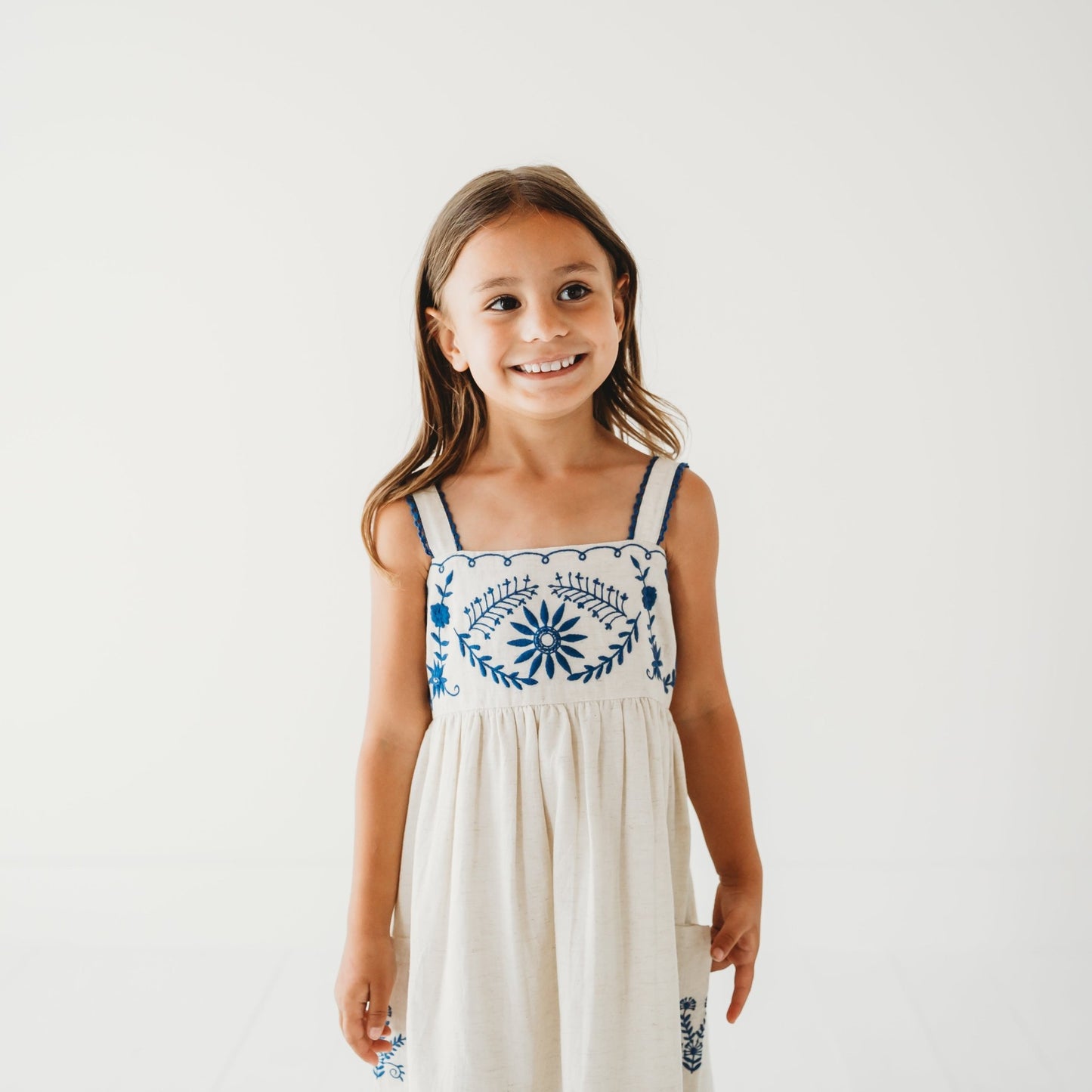 Close up of 5-year-old girl in LARILI Azurea dress. Hand-embroidered linen with lace straps and pockets. Sustainable artisan design.