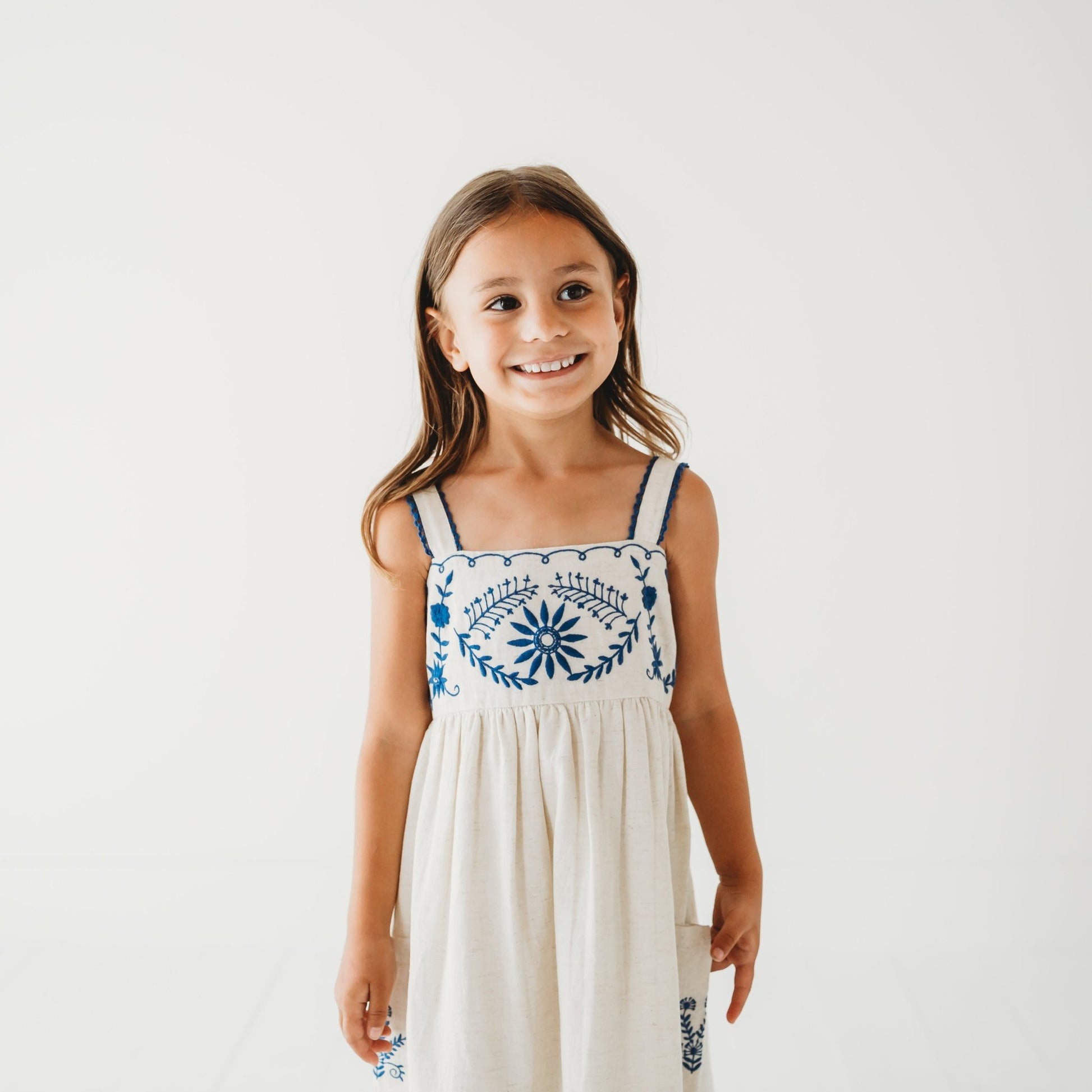 Close up of 5-year-old girl in LARILI Azurea dress. Hand-embroidered linen with lace straps and pockets. Sustainable artisan design.