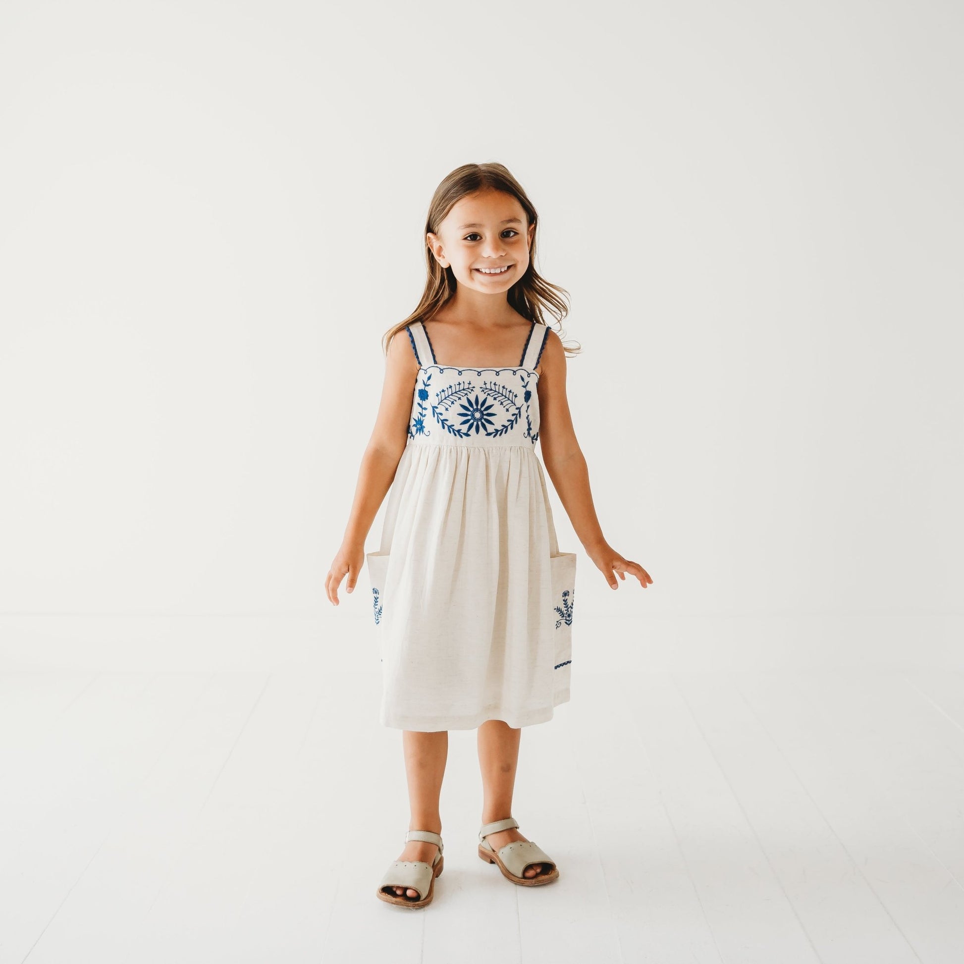 5-year-old girl in LARILI Azurea dress. Hand-embroidered linen with lace straps and pockets. Sustainable artisan design.