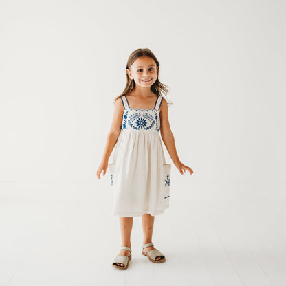 5-year-old girl in LARILI Azurea dress. Hand-embroidered linen with lace straps and pockets. Sustainable artisan design.