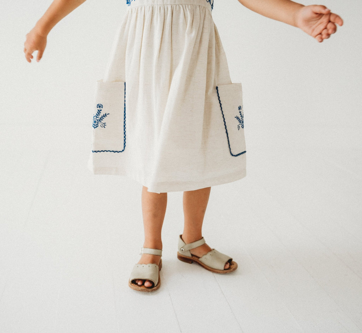 5-year-old girl posing in LARILI Azurea dress. Hand-embroidered linen with lace straps and pockets. Sustainable artisan design.