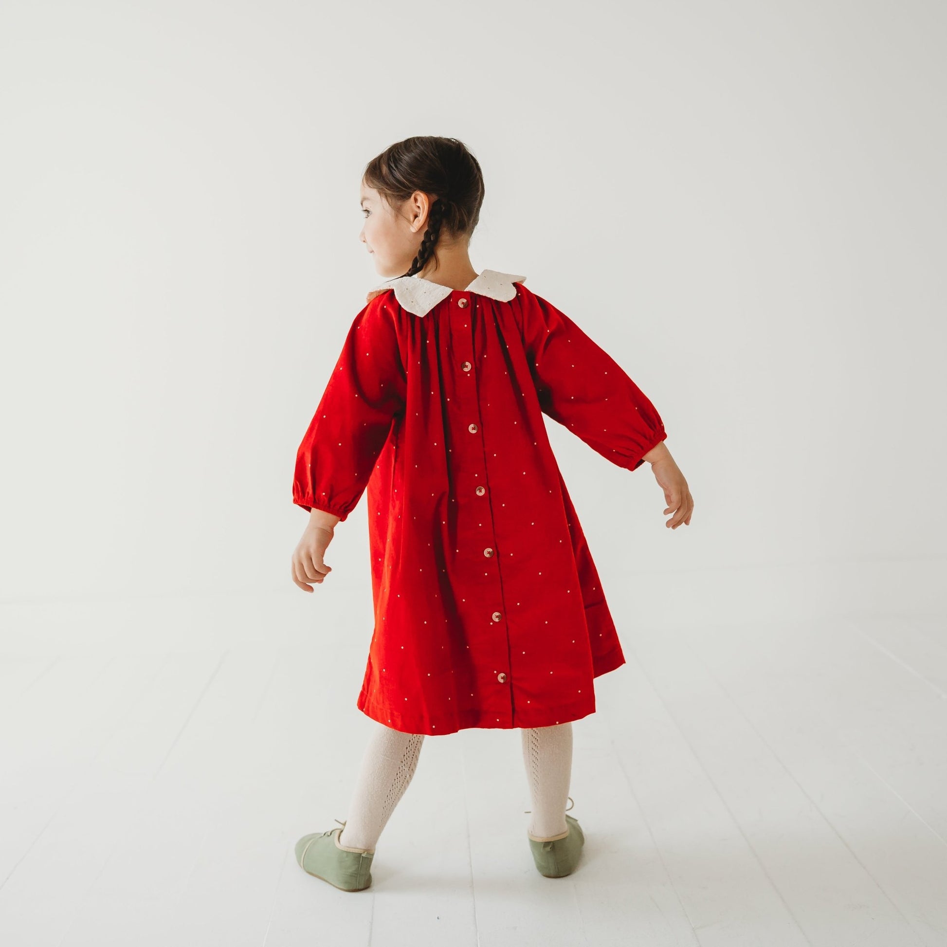 Back view of Girl in LARILI Christmas Carol Red Corduroy Dress with scalloped embroidered collar in a holiday setting.