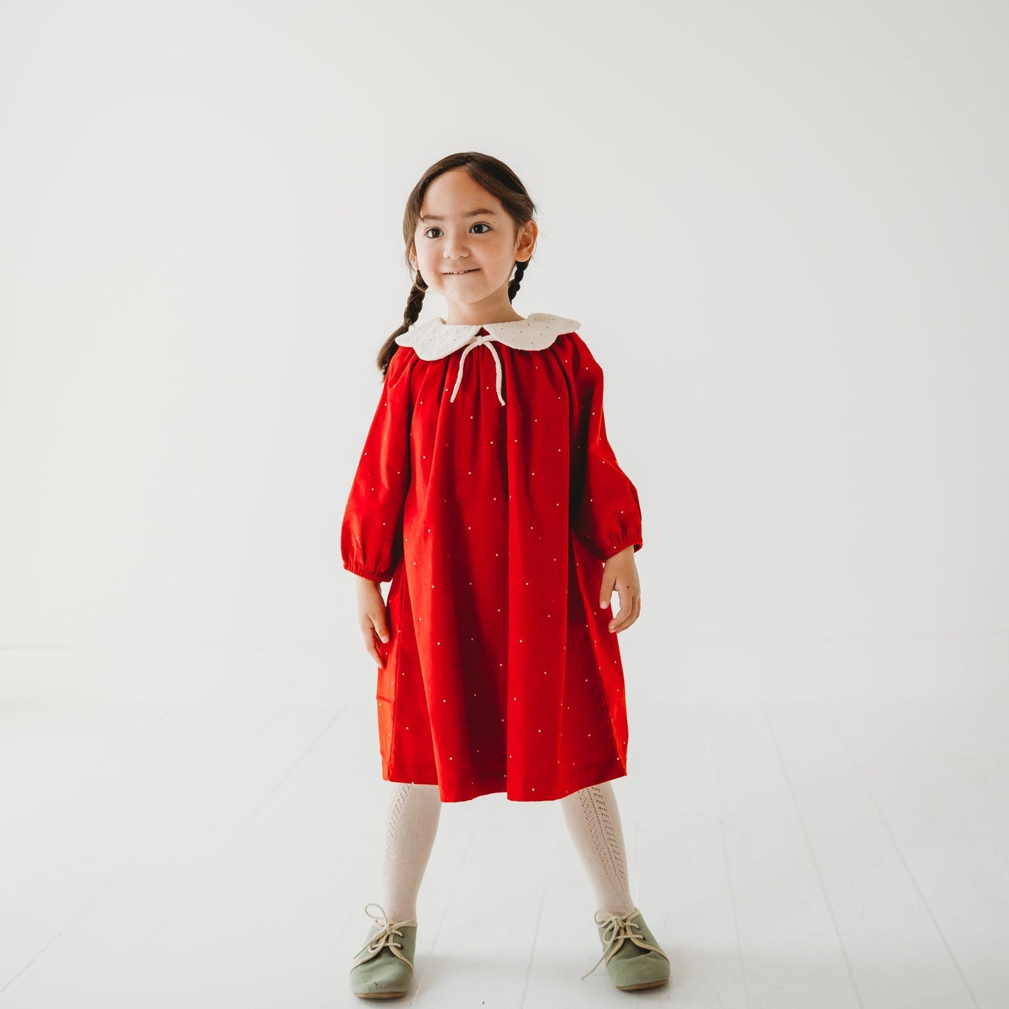 Girl in LARILI Christmas Carol Red Corduroy Dress with scalloped embroidered collar in a holiday setting.