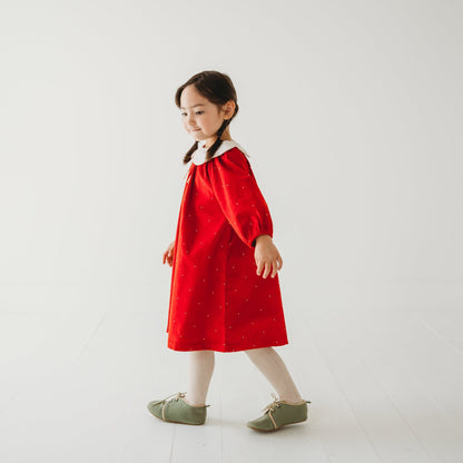 Side pose Girl in LARILI Christmas Carol Red Corduroy Dress with scalloped embroidered collar in a holiday setting.