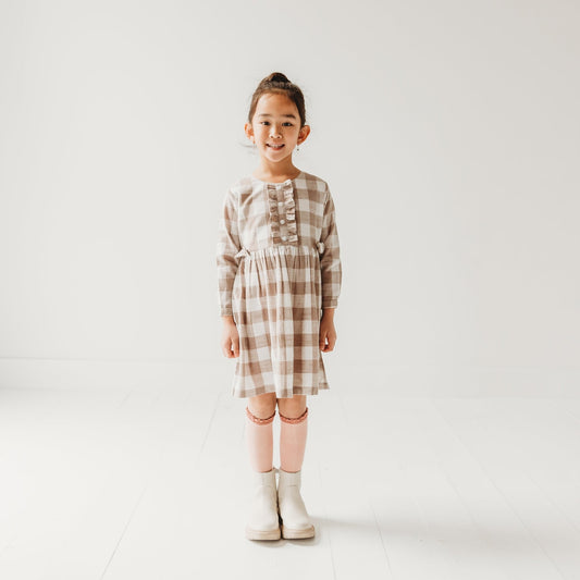 5-year-old girl in LARILI grey gingham dress. Brushed cotton with ruffles, bows, and cuffed collars. Handcrafted design.