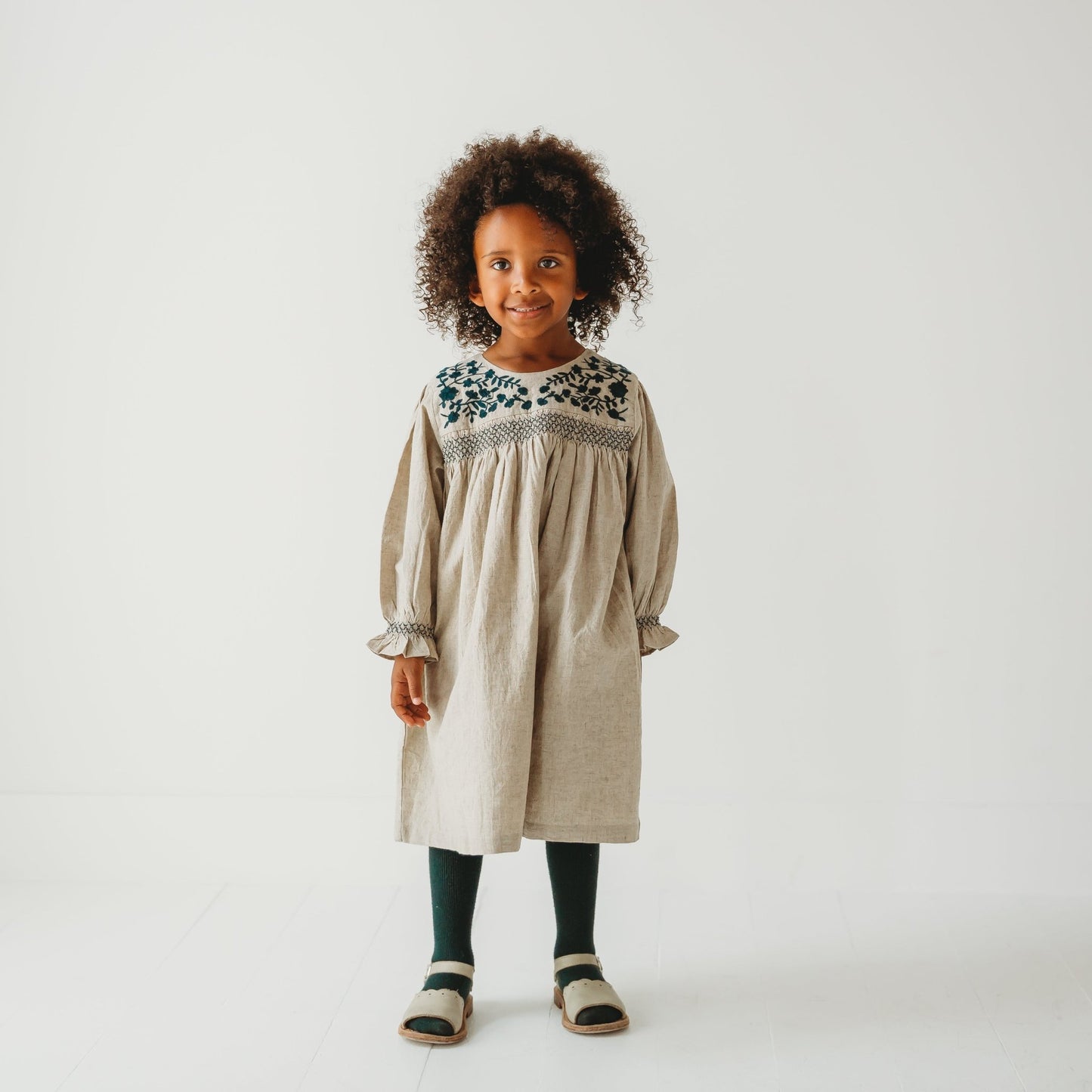 Young girl modeling the Meadow Breeze linen dress with floral embroidery. Artisan girls' fashion by LARILI.