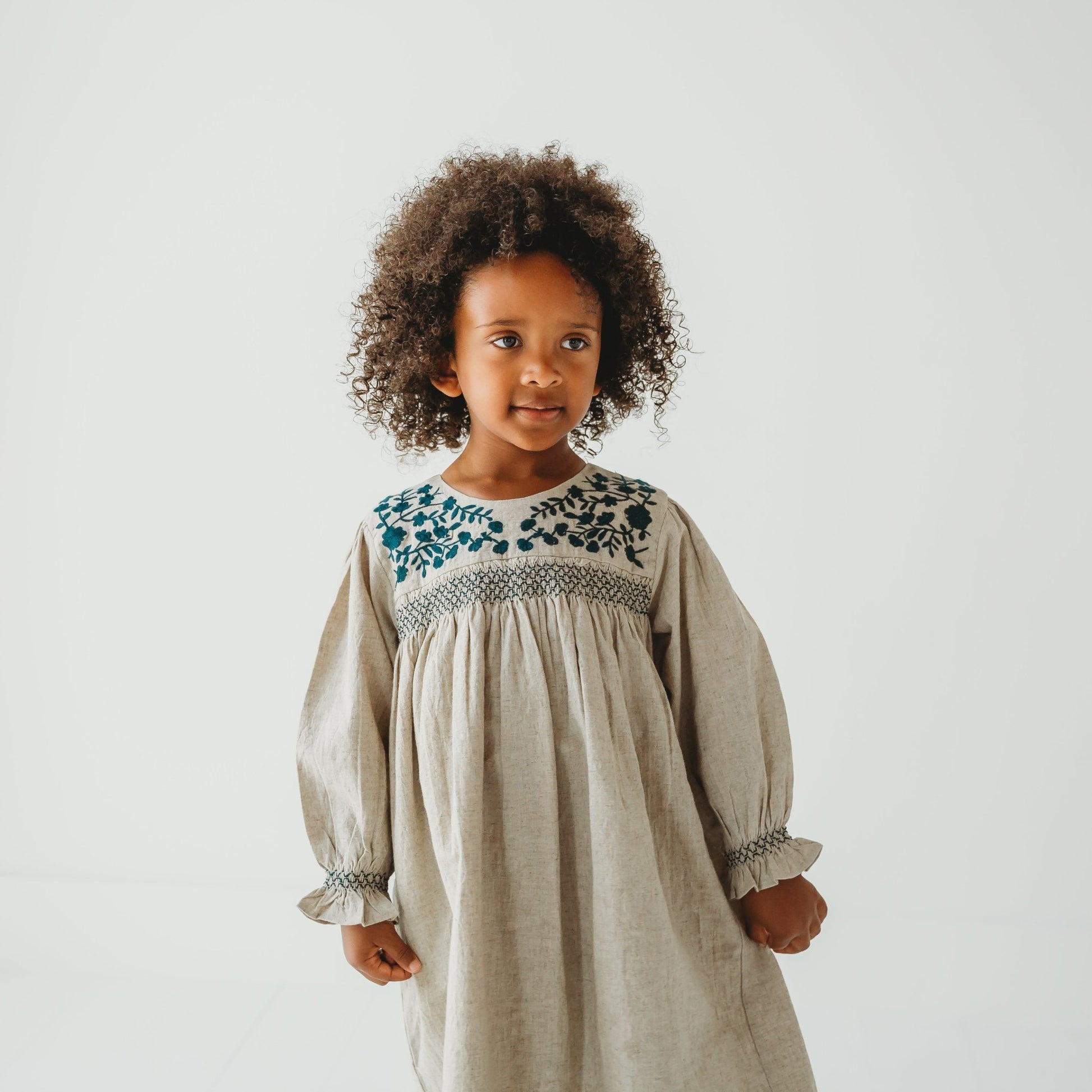 Close up view Young girl modeling the Meadow Breeze linen dress with floral embroidery. Artisan girls' fashion by LARILI.