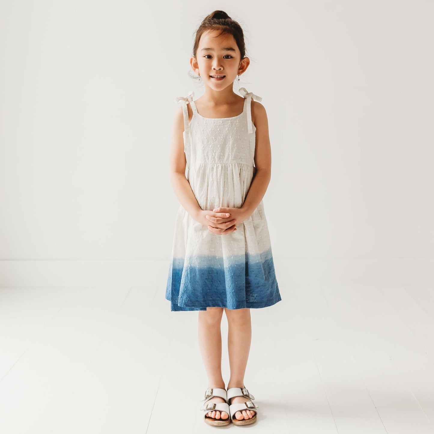 5-year-old girl posing in LARILI ocean ombre dress. Blue gradient 100% cotton Schiffli fabric with nautical embroidery.