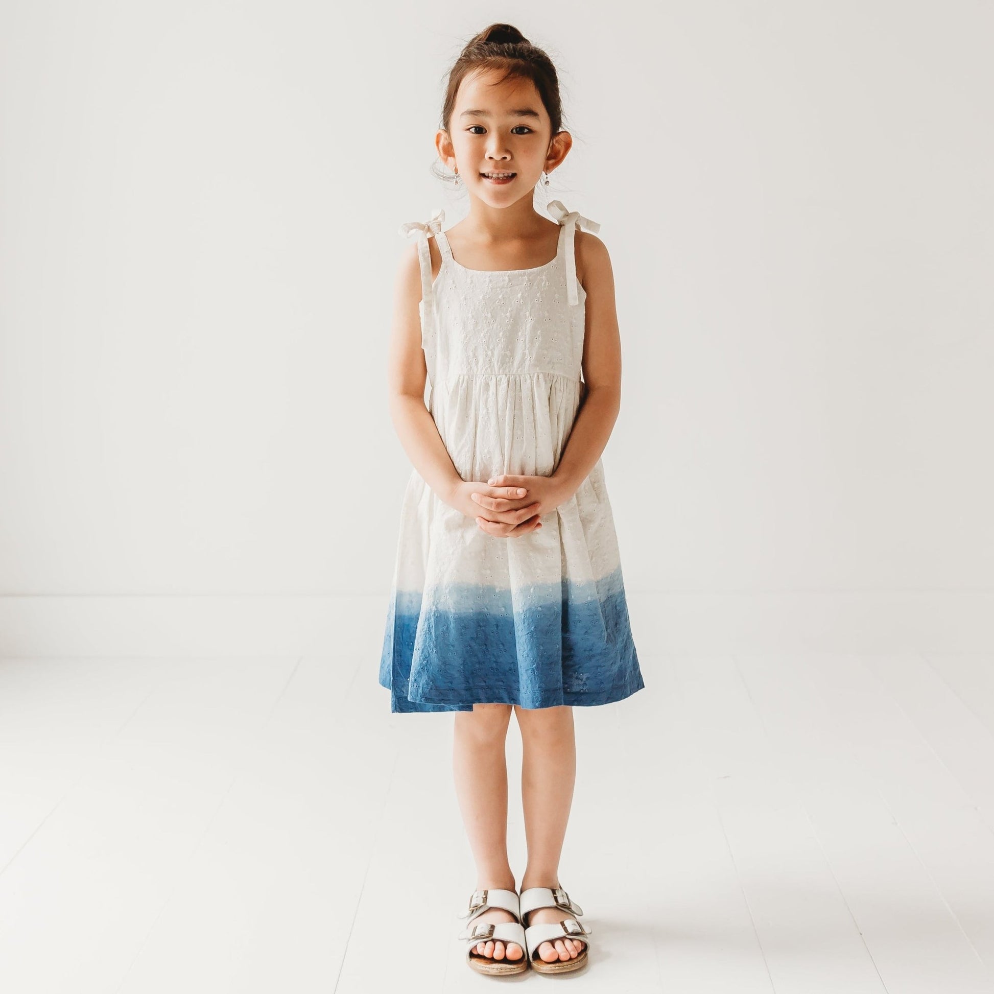 5-year-old girl posing in LARILI ocean ombre dress. Blue gradient 100% cotton Schiffli fabric with nautical embroidery.