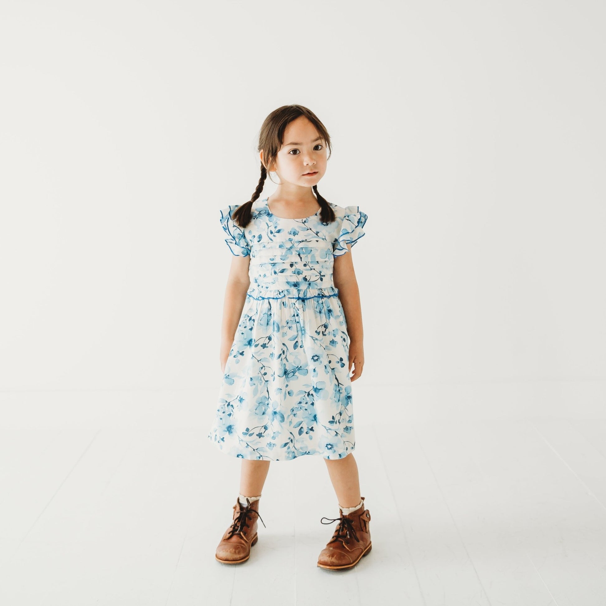 A young girl modeling a periwinkle blue floral rayon dress with double flutter sleeves and a white pintuck yoke.