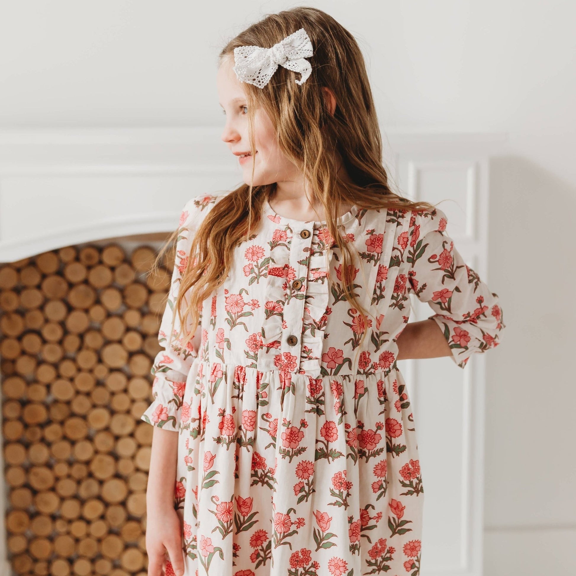 Young girl sitting and smiling, wearing the Pink Block Print Flower dress. Detailed view of the artisan floral pattern.