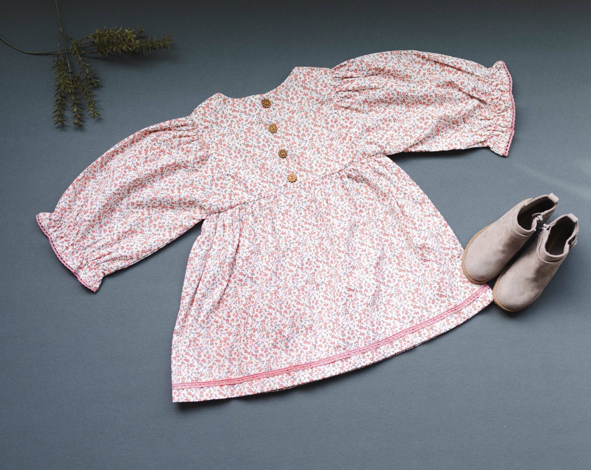 Overhead back view of the LARILI pink ditsy print corduroy dress, highlighting the soft fabric texture, floral patterns, and lace detailing and wooden buttons.