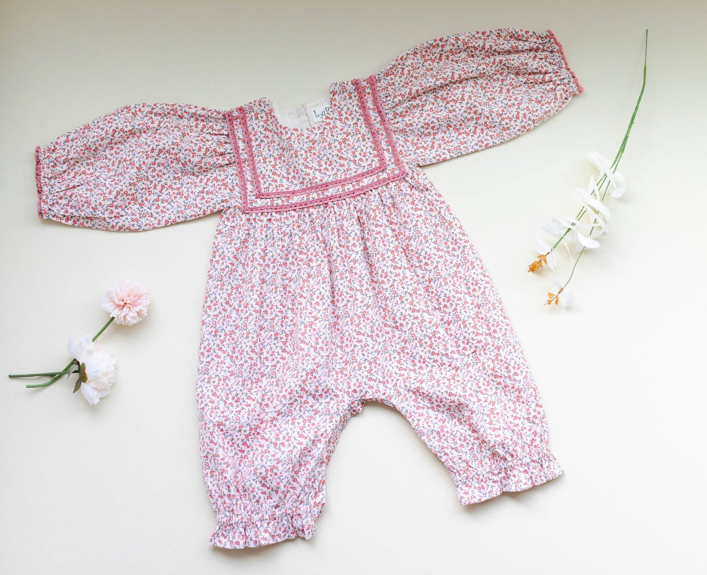 Overhead view of soft pink corduroy romper, showing ditsy print and delicate lace. Vintage-style baby fashion.