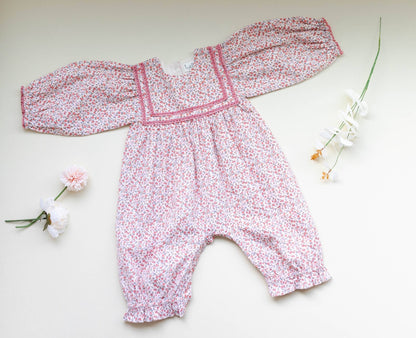 Overhead view of soft pink corduroy romper, showing ditsy print and delicate lace. Vintage-style baby fashion.