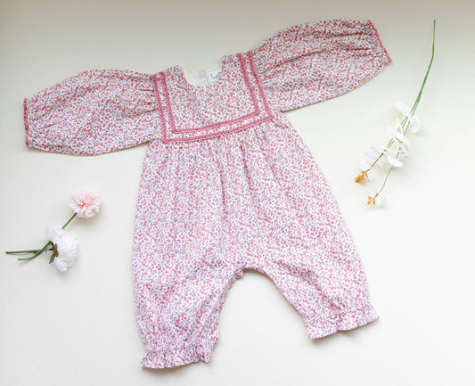 Overhead view of soft pink corduroy romper, showing ditsy print and delicate lace. Vintage-style baby fashion.