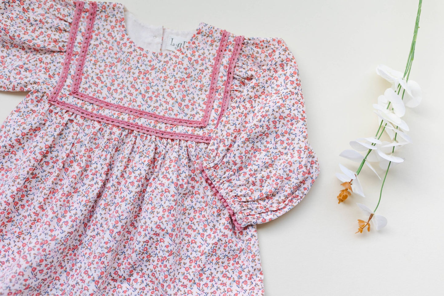Close up view of soft pink corduroy romper, showing ditsy print and delicate lace. Vintage-style baby fashion