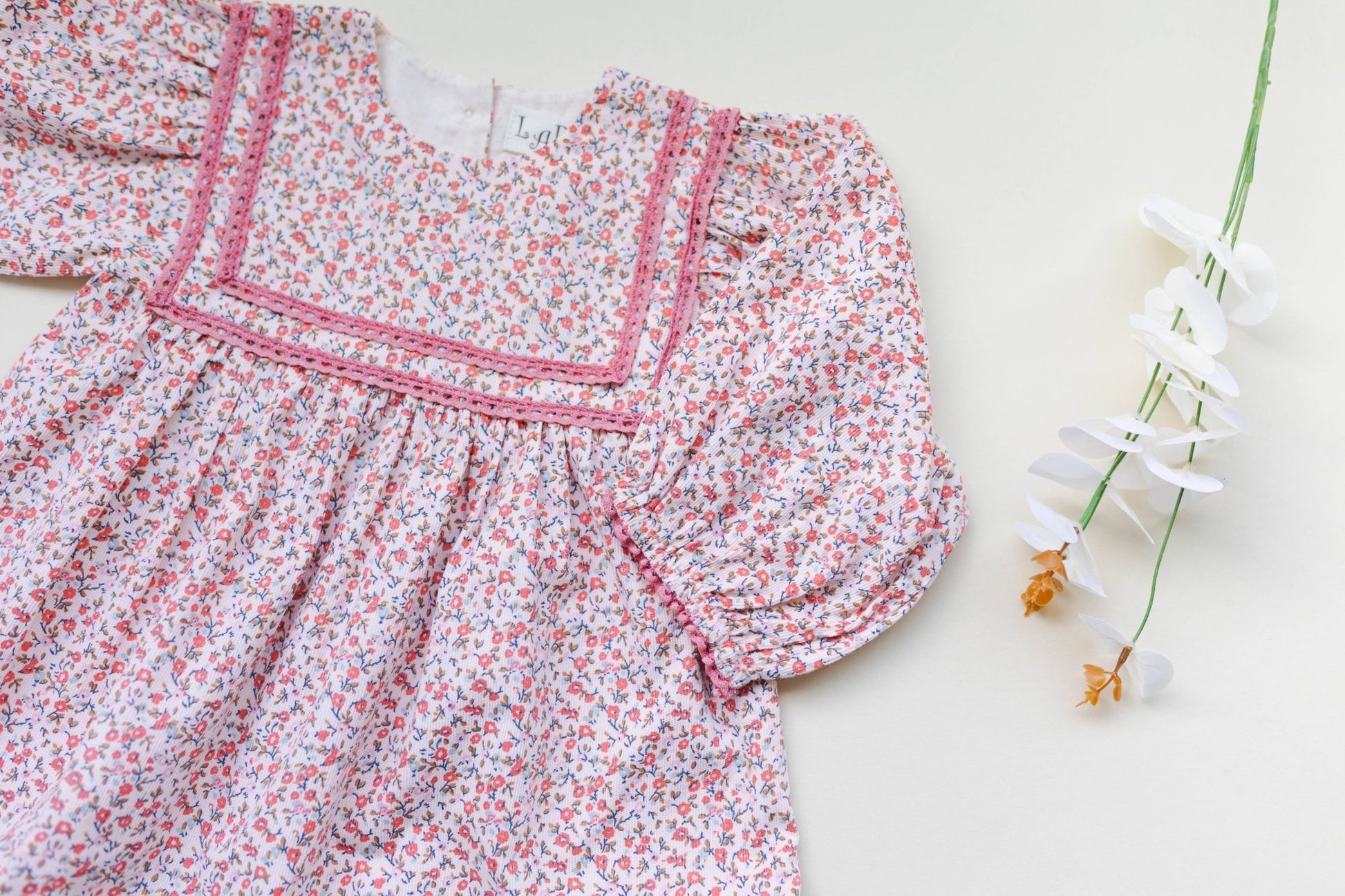 Close up view of soft pink corduroy romper, showing ditsy print and delicate lace. Vintage-style baby fashion