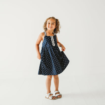 5-year-old girl posing in LARILI nautical blue polka dot dress. 100% cotton with lace straps and vintage button details.