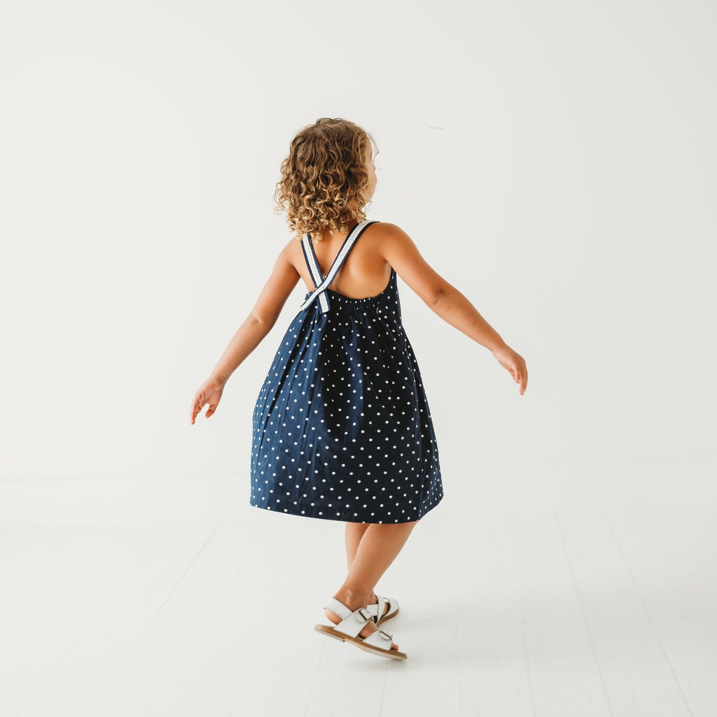 Back View of 5-year-old girl in LARILI nautical blue polka dot dress. 100% cotton with lace straps and vintage button details