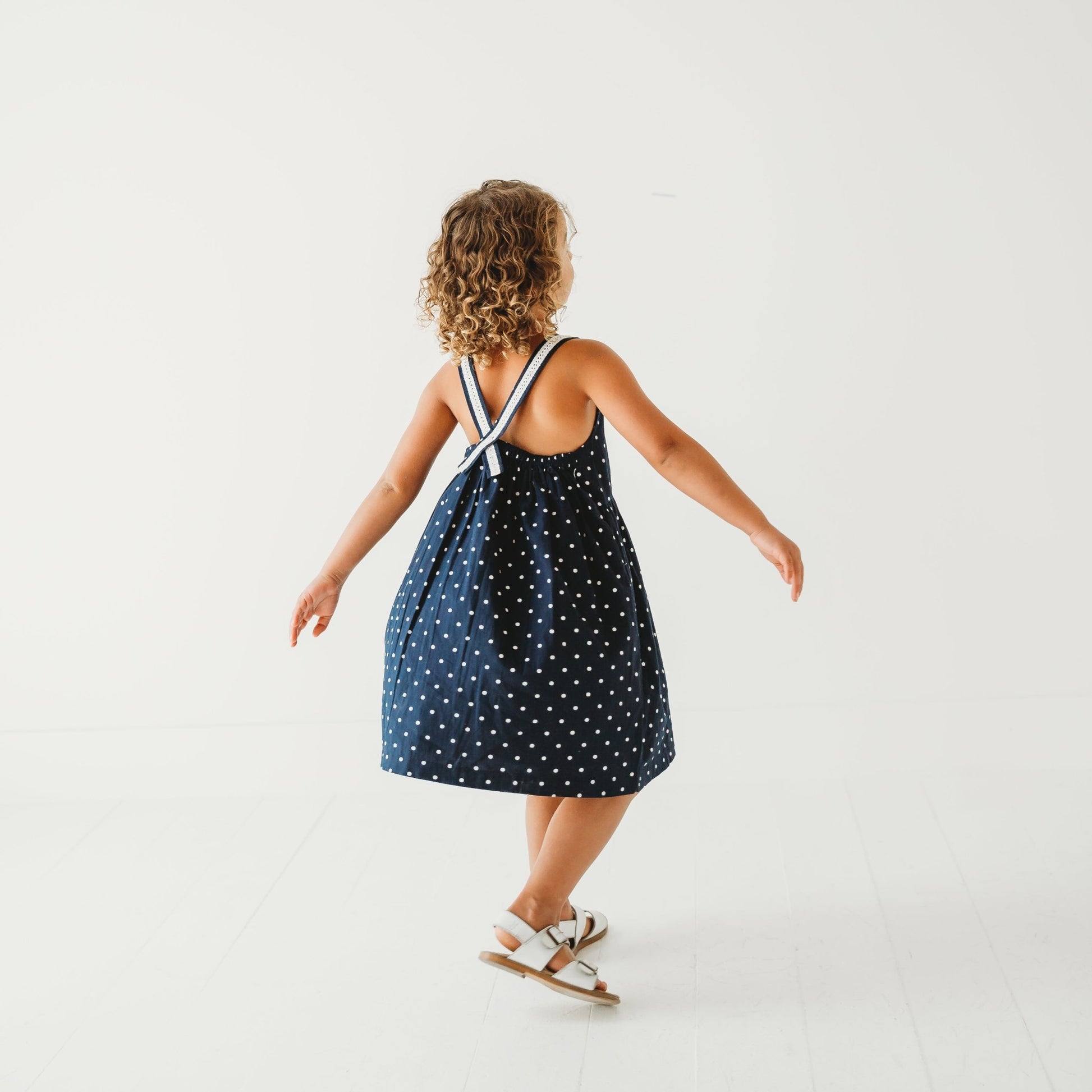 Back View of 5-year-old girl in LARILI nautical blue polka dot dress. 100% cotton with lace straps and vintage button details